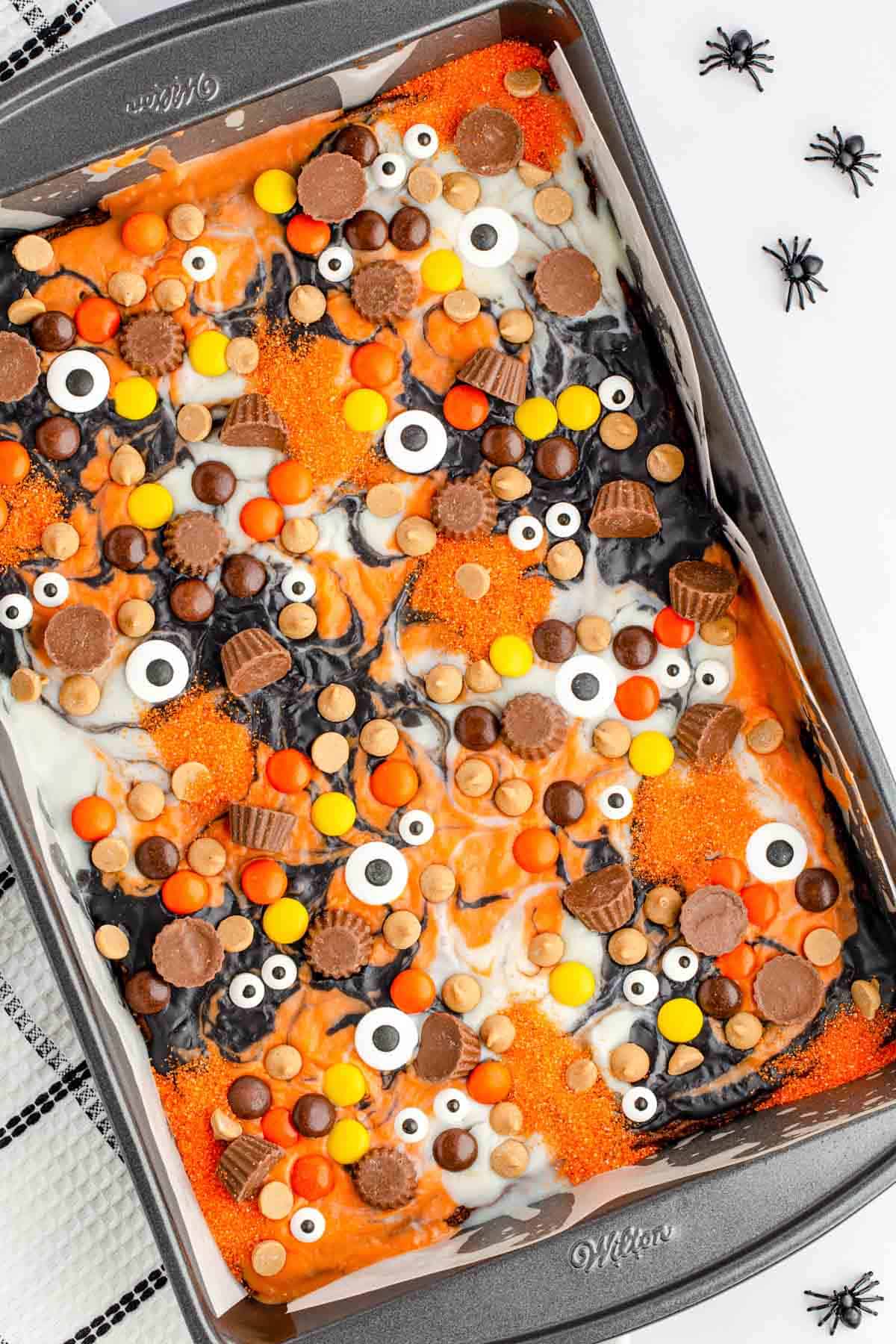 A baking pan of brownies topped with festive eyeball candies and peanut butter treats, with colors of orange, black, and white ganache.