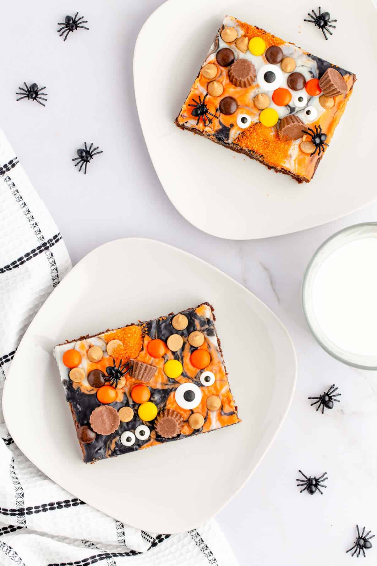 A table set with two plates with slices of peanut butter halloween eyeball brownies set with a glass of milk.