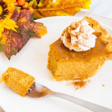 A slice of easy pumpkin pie topped with whipped cream and sprinkled with pumpkin pie spice with a bite removed on a fork.