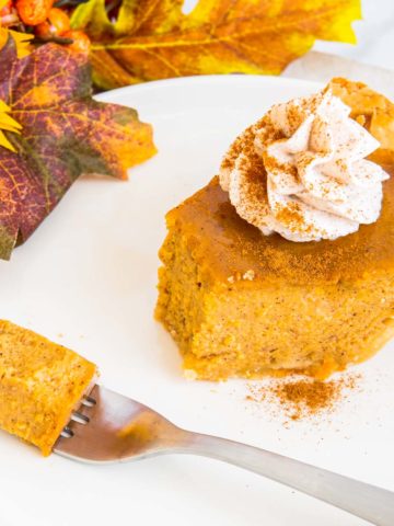 A slice of easy pumpkin pie topped with whipped cream and sprinkled with pumpkin pie spice with a bite removed on a fork.