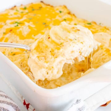 A spoonful of au gratin potatoes being scooped out of a white casserole dish.