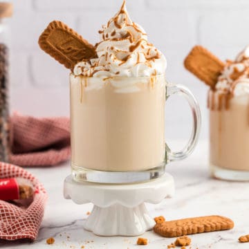 A glass coffee cup with a Biscoff Latte set on a white pedestal with scatter crumbs at the bottom.