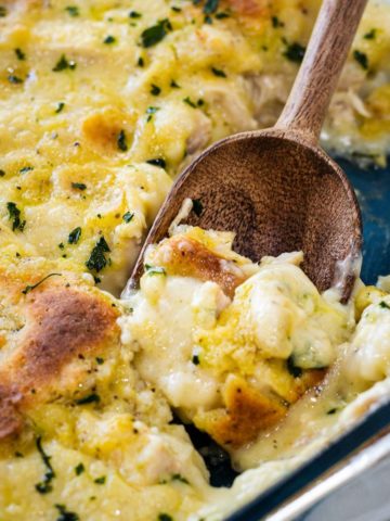Chicken and dumplings in a clear casserole dish with a scoop being removed with a wooden spoon.
