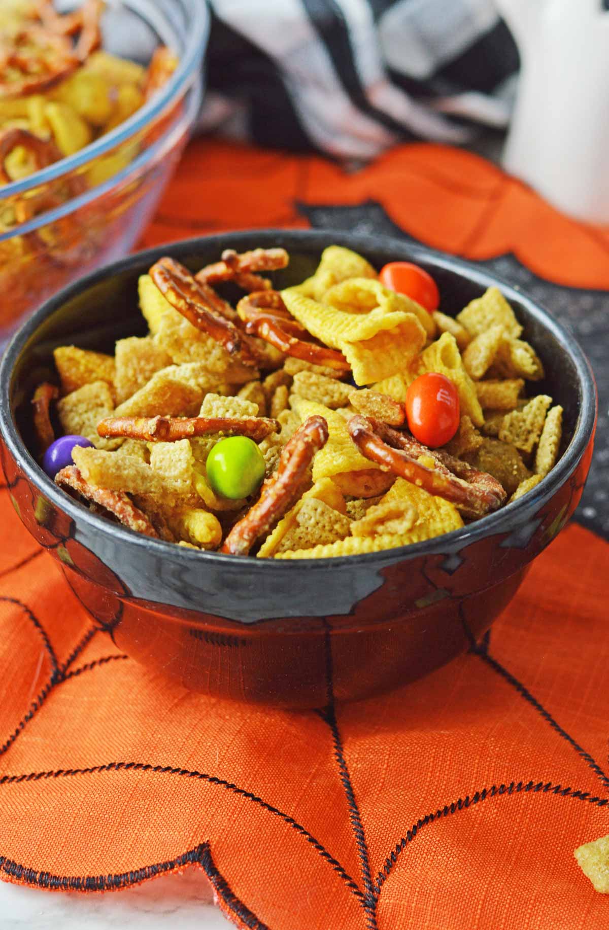 A black bowl full of Halloween Chex Mix set on an orange halloween placemat.