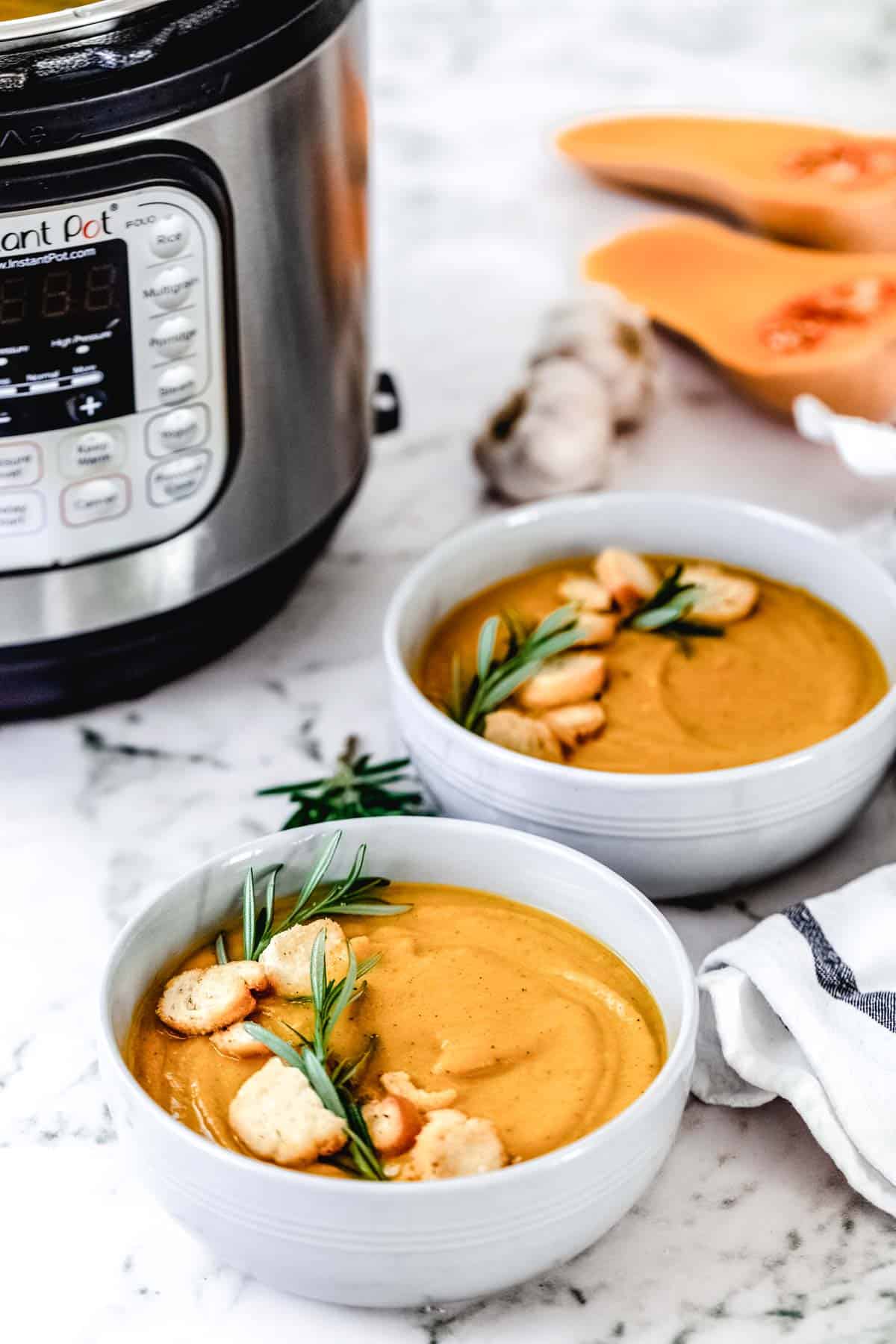 Two white bowls filled with Instant Pot Butternut Squash Soup with an instant pot in the background.