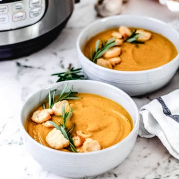 Two white bowls filled with Instant Pot Butternut Squash Soup with an instant pot in the background.