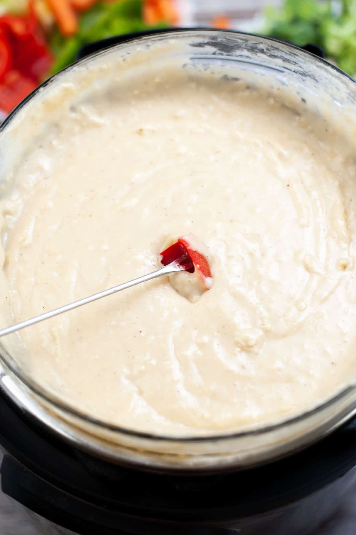 A skewer with a sliced red pepper being dipped into cheese fondue in a instant pot.