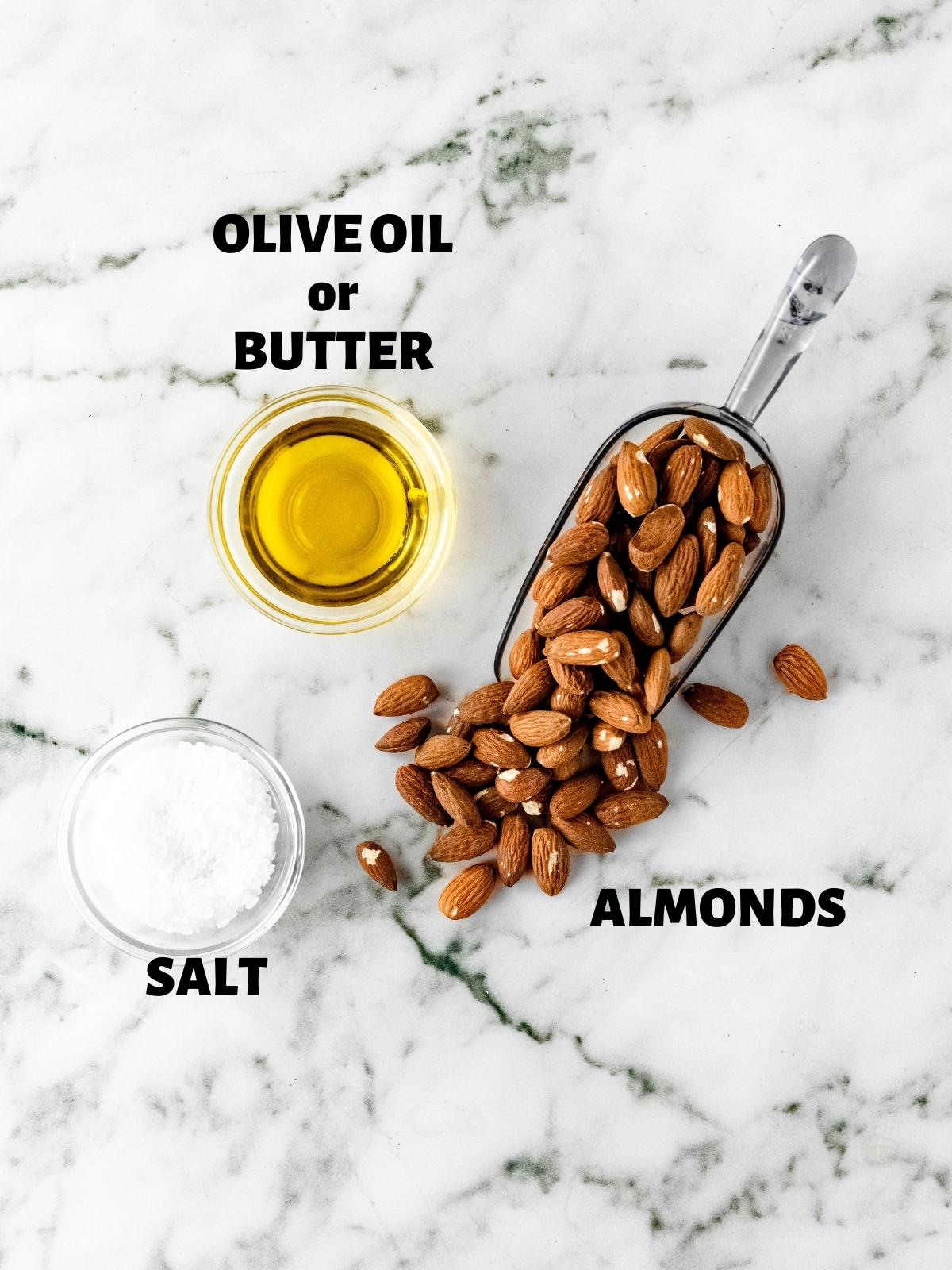 A marble table with a scoop full of almonds, a bowl of olive oil, and a bowl of salt.
