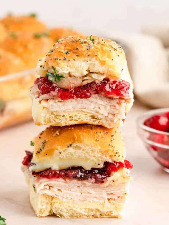 Two cranberry turkey sliders stacked on top of each other with a bowl of cranberries and the dish of sliders in the background.