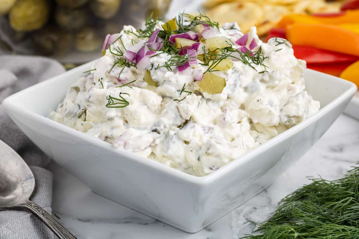 A white dish filled with pickle dip with a spoon to the side set on a marble table.