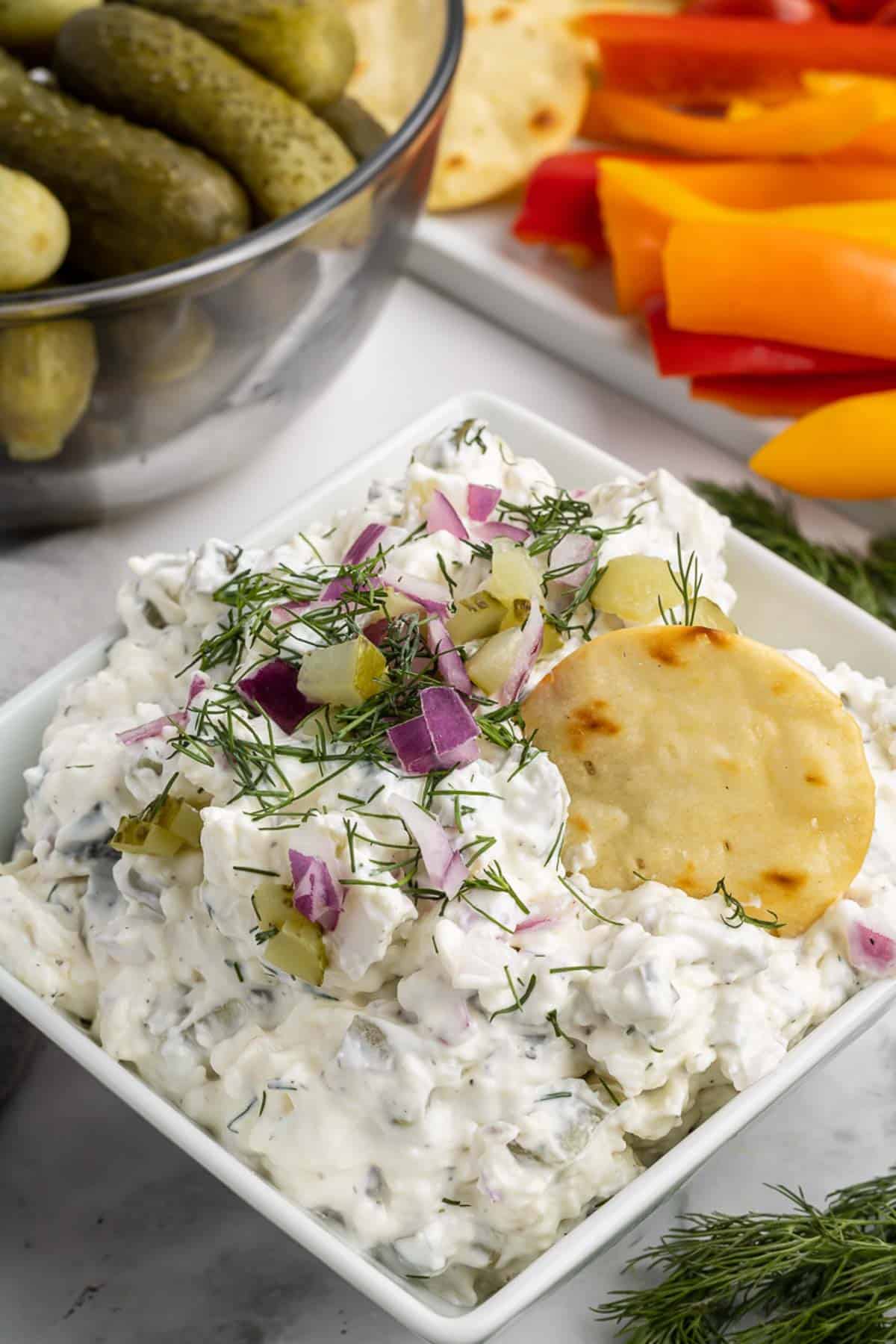 A bowl of pickle dip with a chip dipped into it.