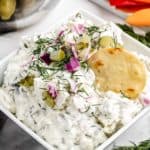 Up close image dill pickle dip with a chip dipped into the top served in a white bowl.