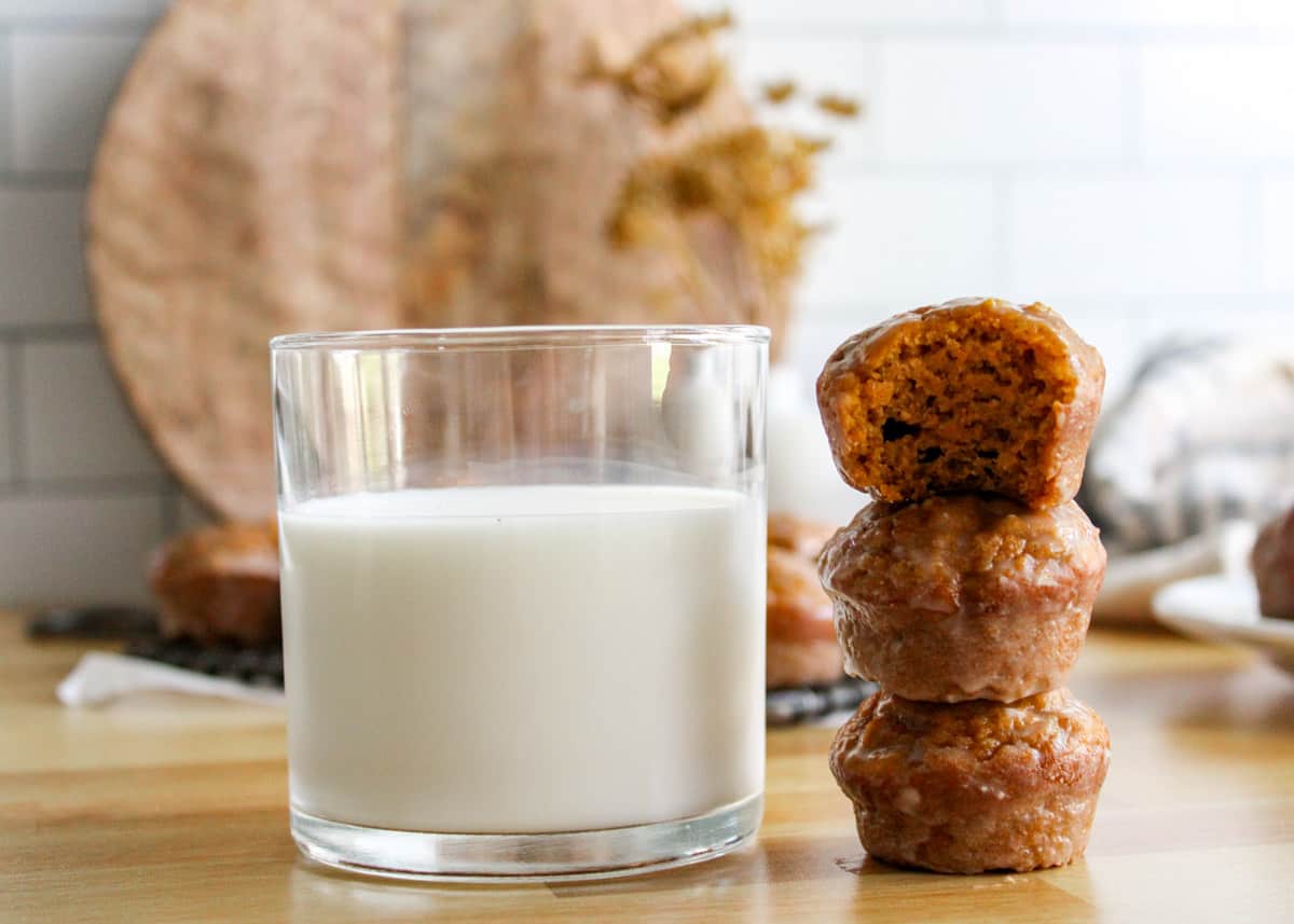 A stack of pumpkin muffins on a wooden table set beside a full glass of milk.