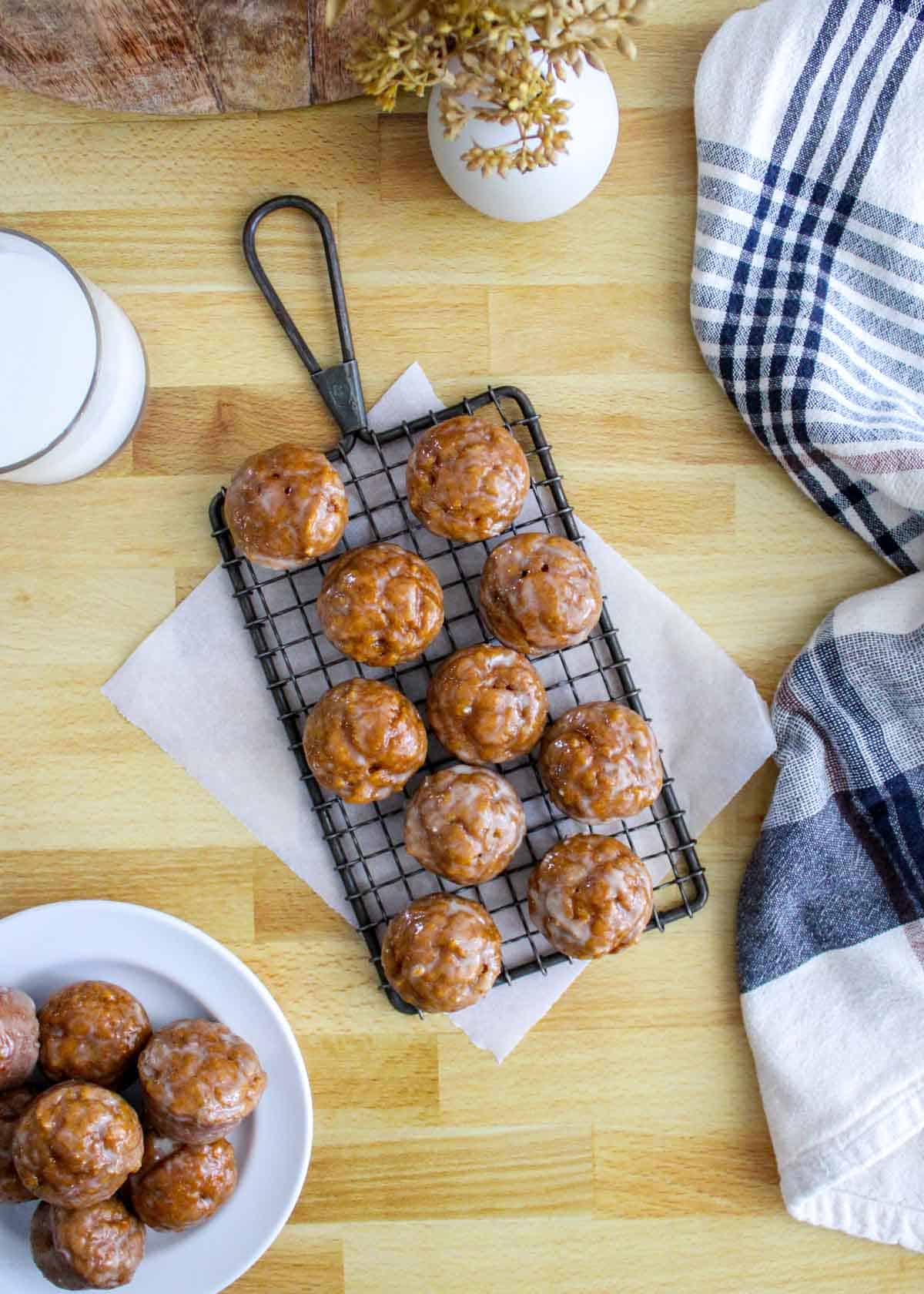 Glazed pumpkin donut muffins setting on a cooling rack after being glazed.