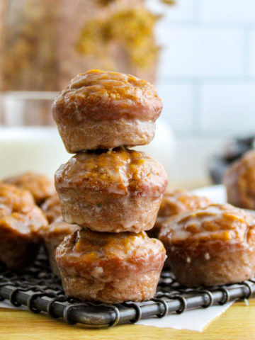 Glazed pumpkin donut muffins on a wire cooling rack stacked three high with muffins surrounding them and a glass of milk in the background.