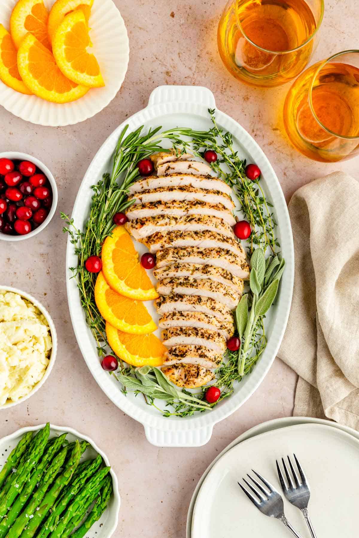 A tablescape filled with sliced turkey, asparagus, mashed potatoes, cranberries and wine.