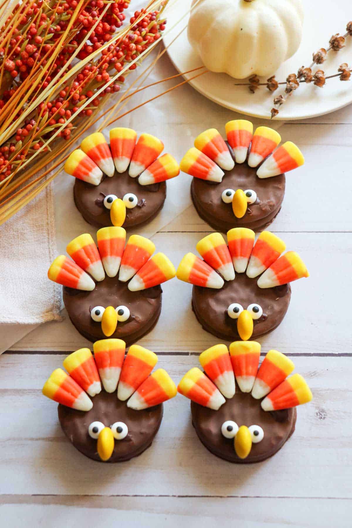 Six Nutter Butter Turkey Cookies on a white wooden plank tray with fall decor in the background.