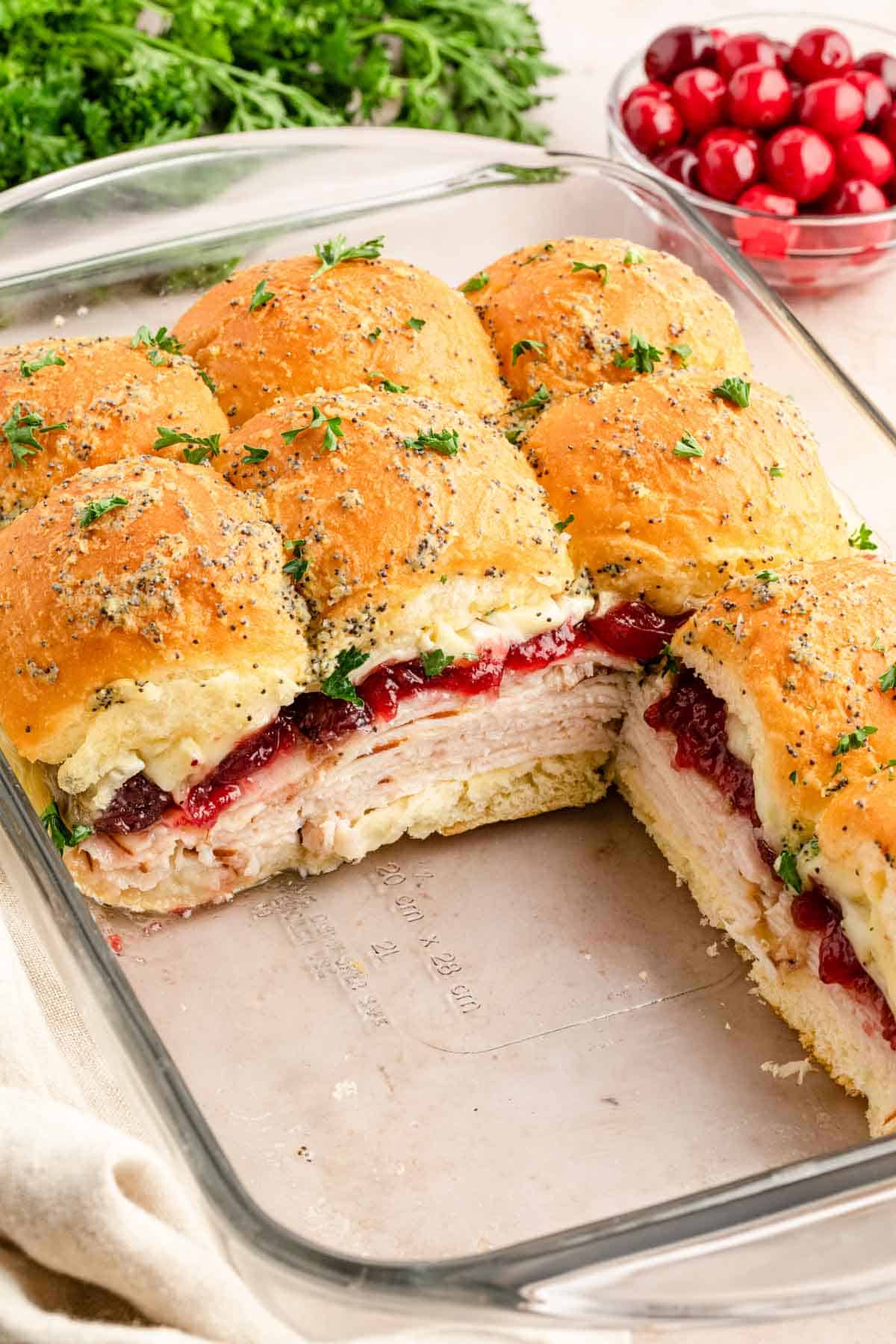 A glass baking pan of turkey slider sandwiches with a few moved from the pan.