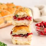 Two cranberry turkey sliders stacked on top of each other with a bowl of cranberries and the dish of sliders in the background.