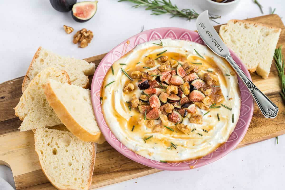 A wooden board with sliced artisan bread an a bowl filled with feta dip.