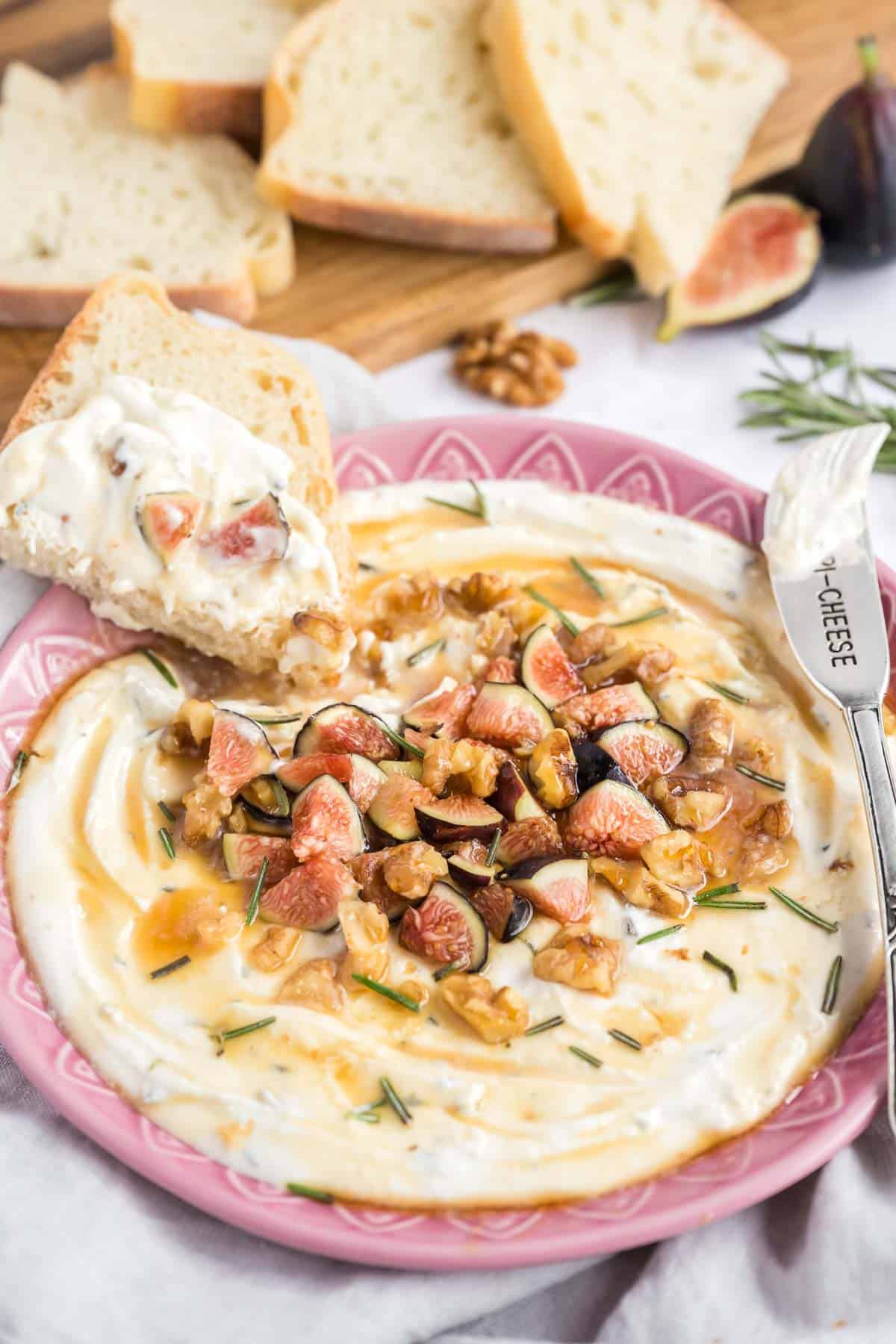 A pink bowl filled with a feta cheese dip with a slice of dipped bread on the bowl.