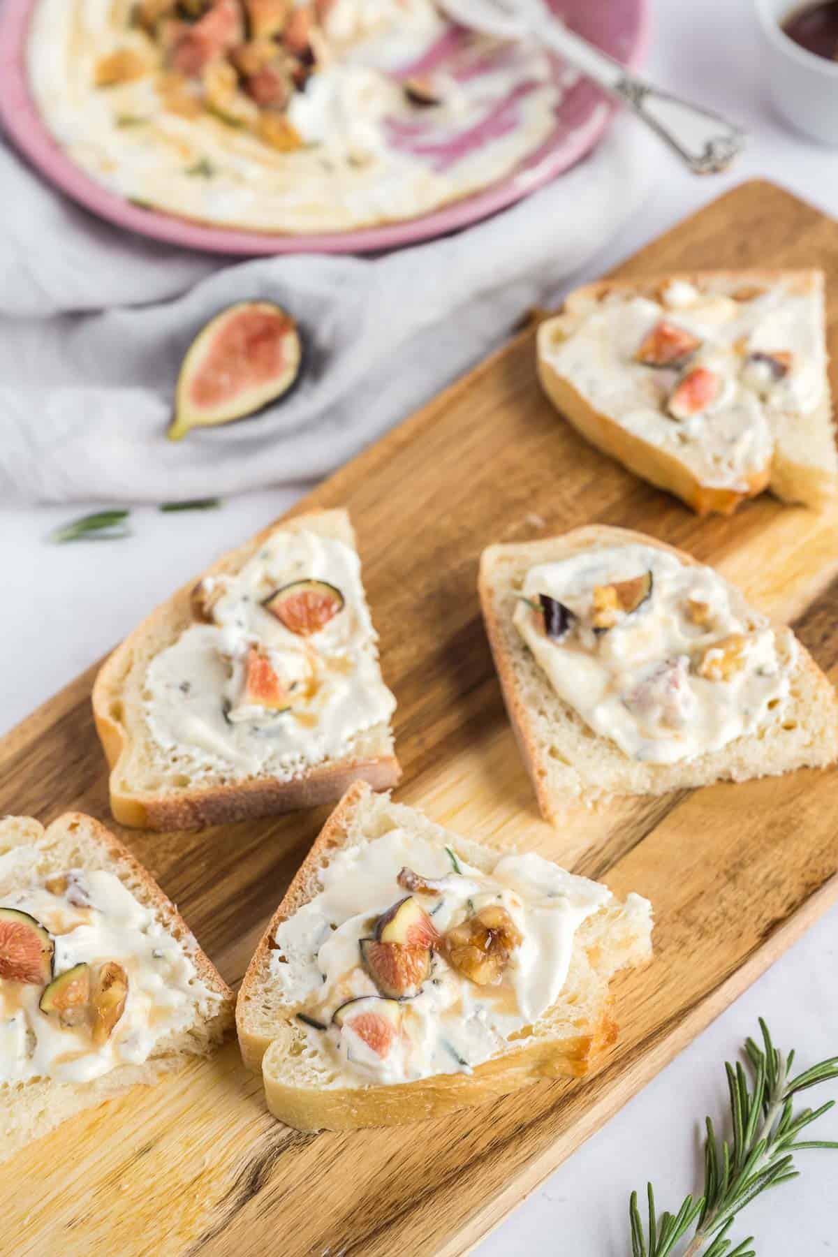 Artisan bread slices smeared with whipped feta dip and garnished with chopped figs and drizzle honey on a wood serving board.