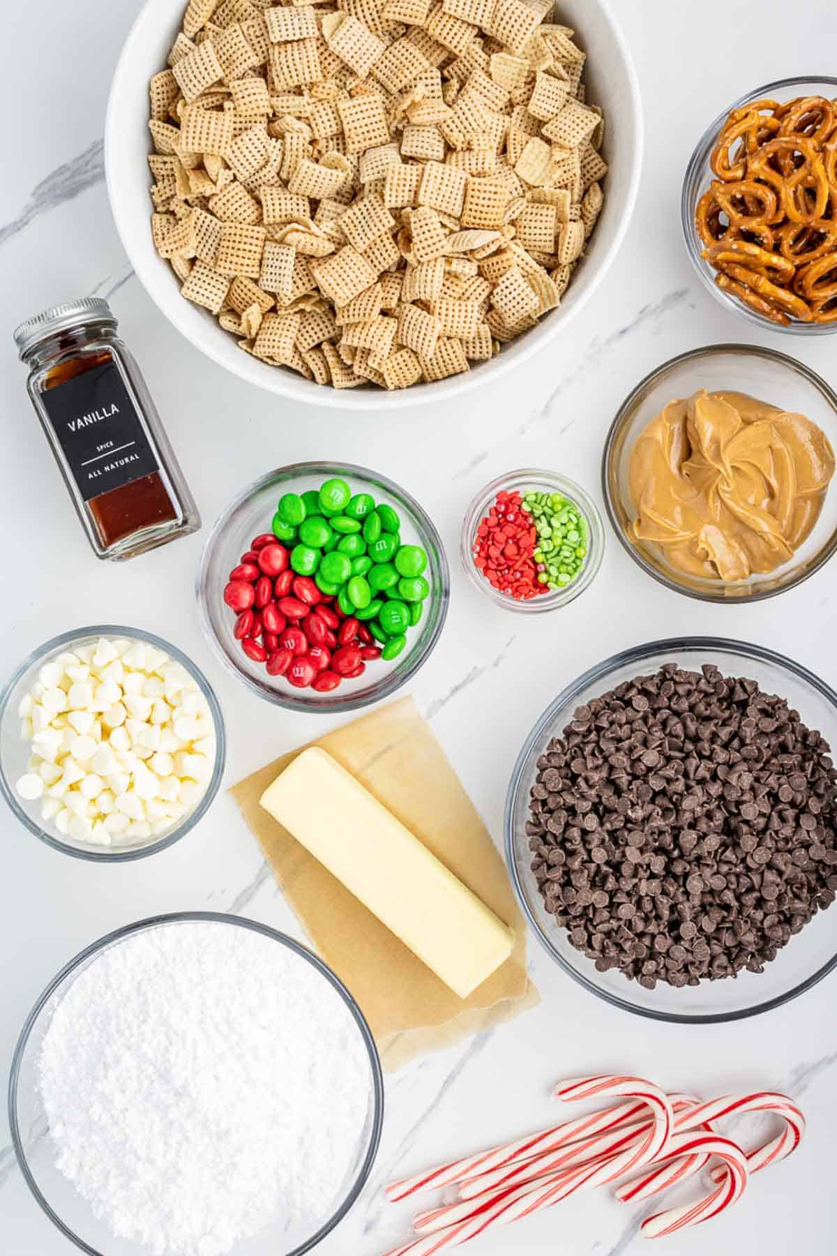 Ingredients needed to make Christmas Muddy Buddies laid out on a marble table.