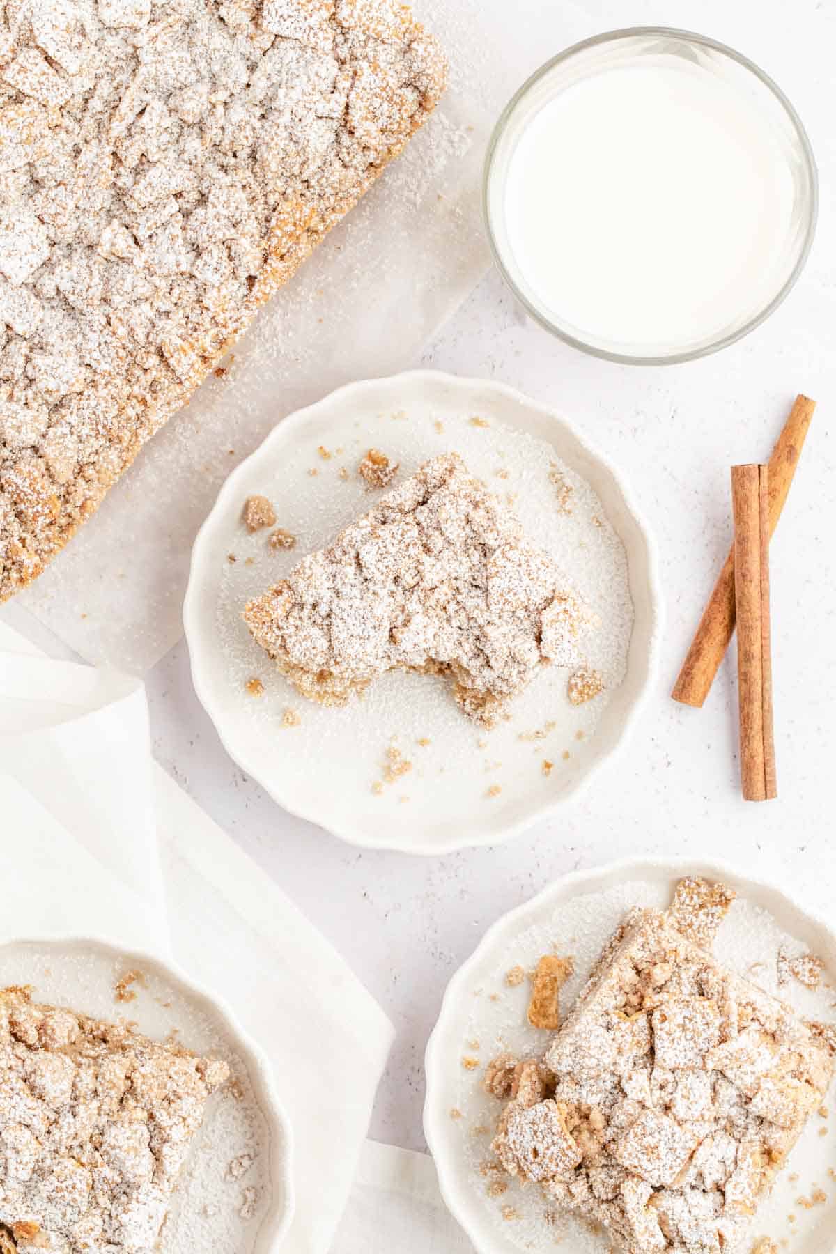 Table set with white plates of cinnamon toast crunch decorated with cinnamon sticks and a cup of milk in the backdrop.