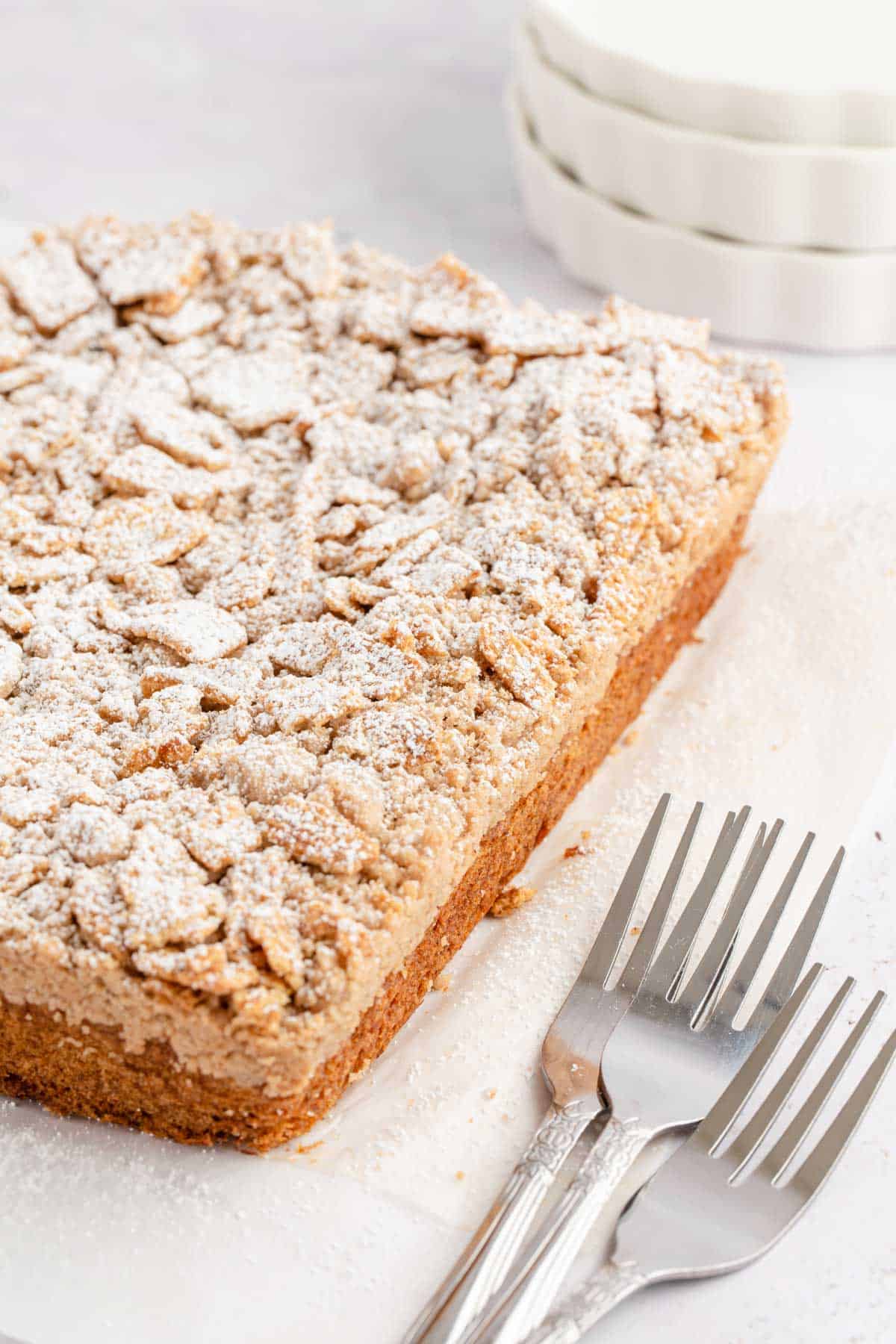 A whole cake dusted with powdered sugar set on parchment paper with 3 forks stacked to the side of the cake.