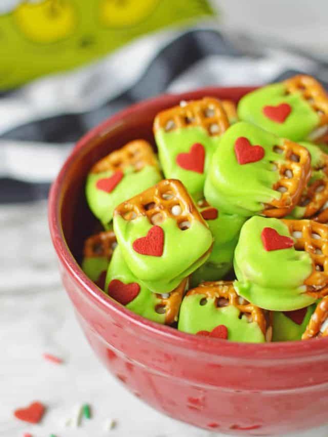 An up close shot of the grinch pretzels in a bowl with sprinkles scattered on the table beside them.