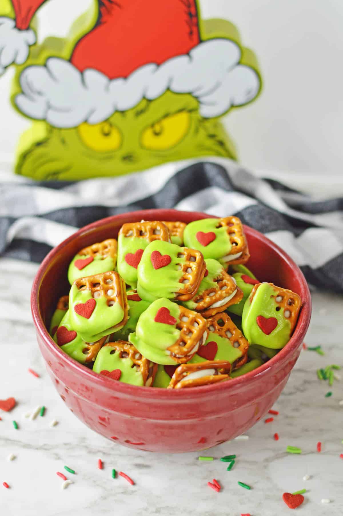 A red bowl filled with Grinch pretzel bites with a grinch face in the background.