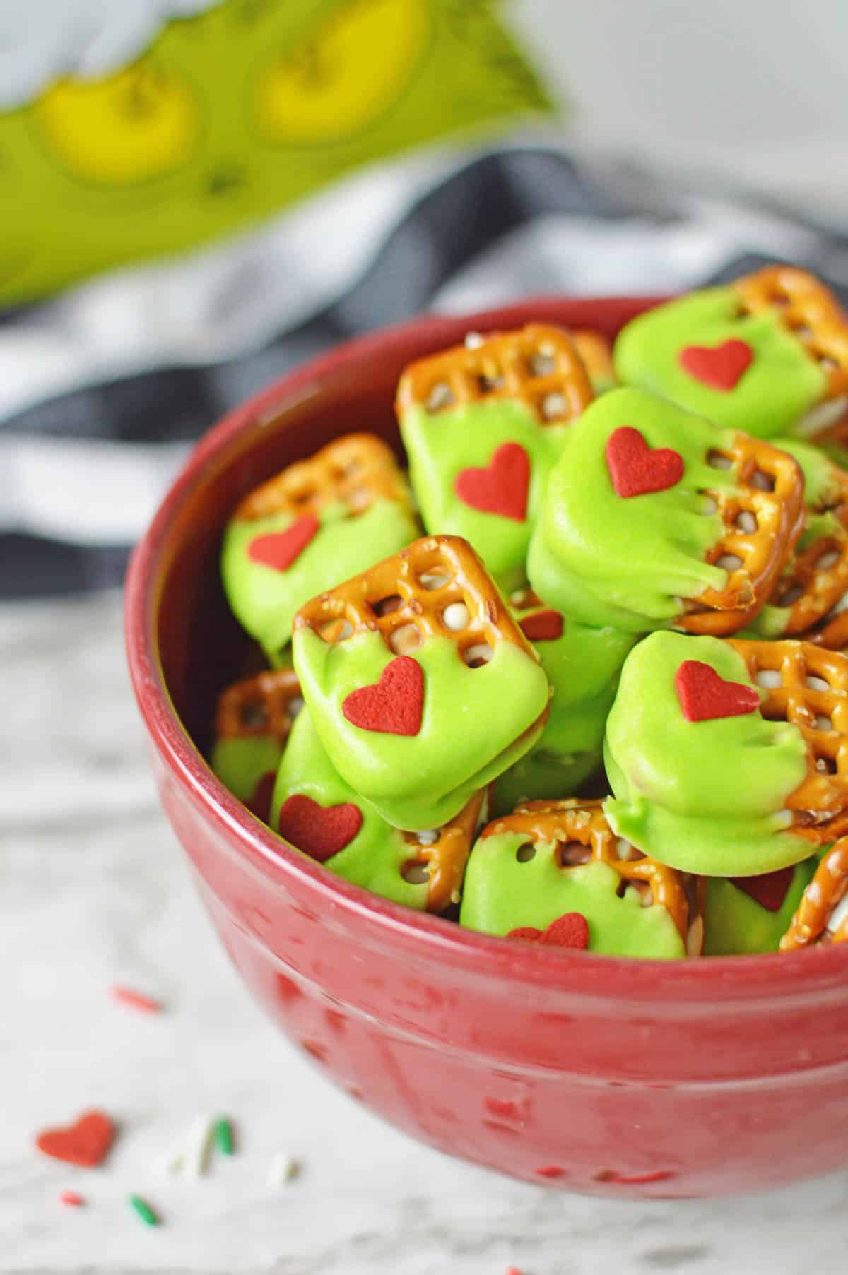 An up close shot of the grinch pretzels in a bowl with sprinkles scattered on the table beside them.