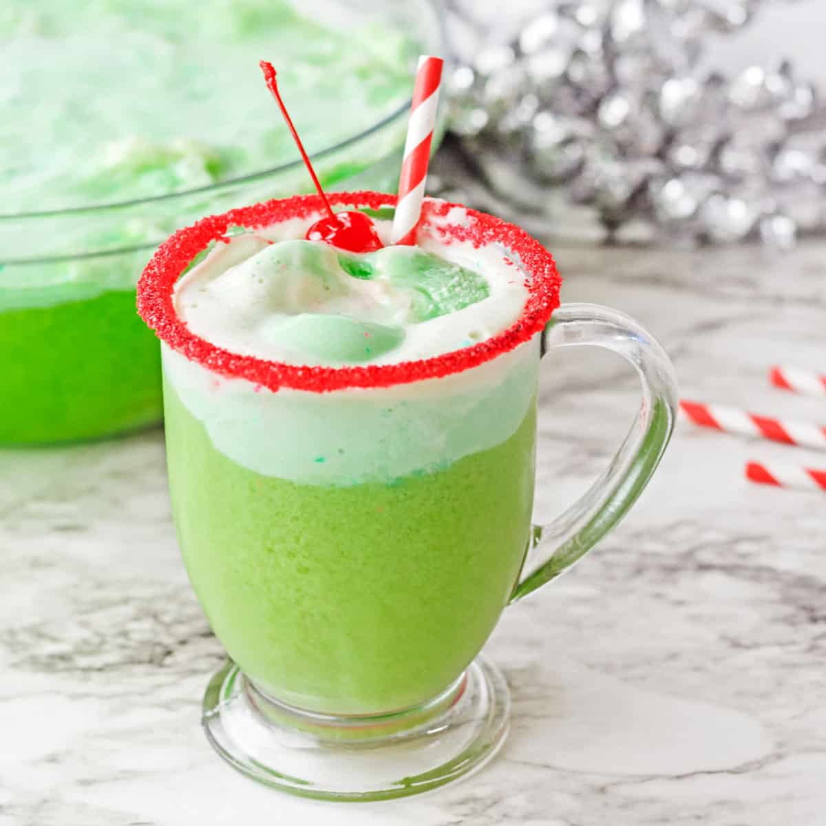 Grinch Punch in a clear glass with a red sugar rim garnished with a cherry.