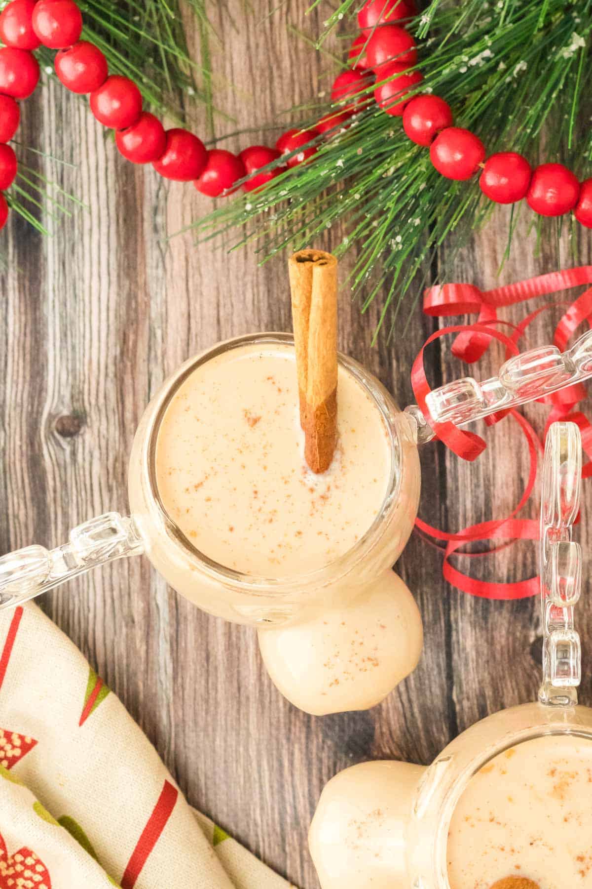 An overhead shot of a cup of eggnog on a wooden table with festive Christmas decor.