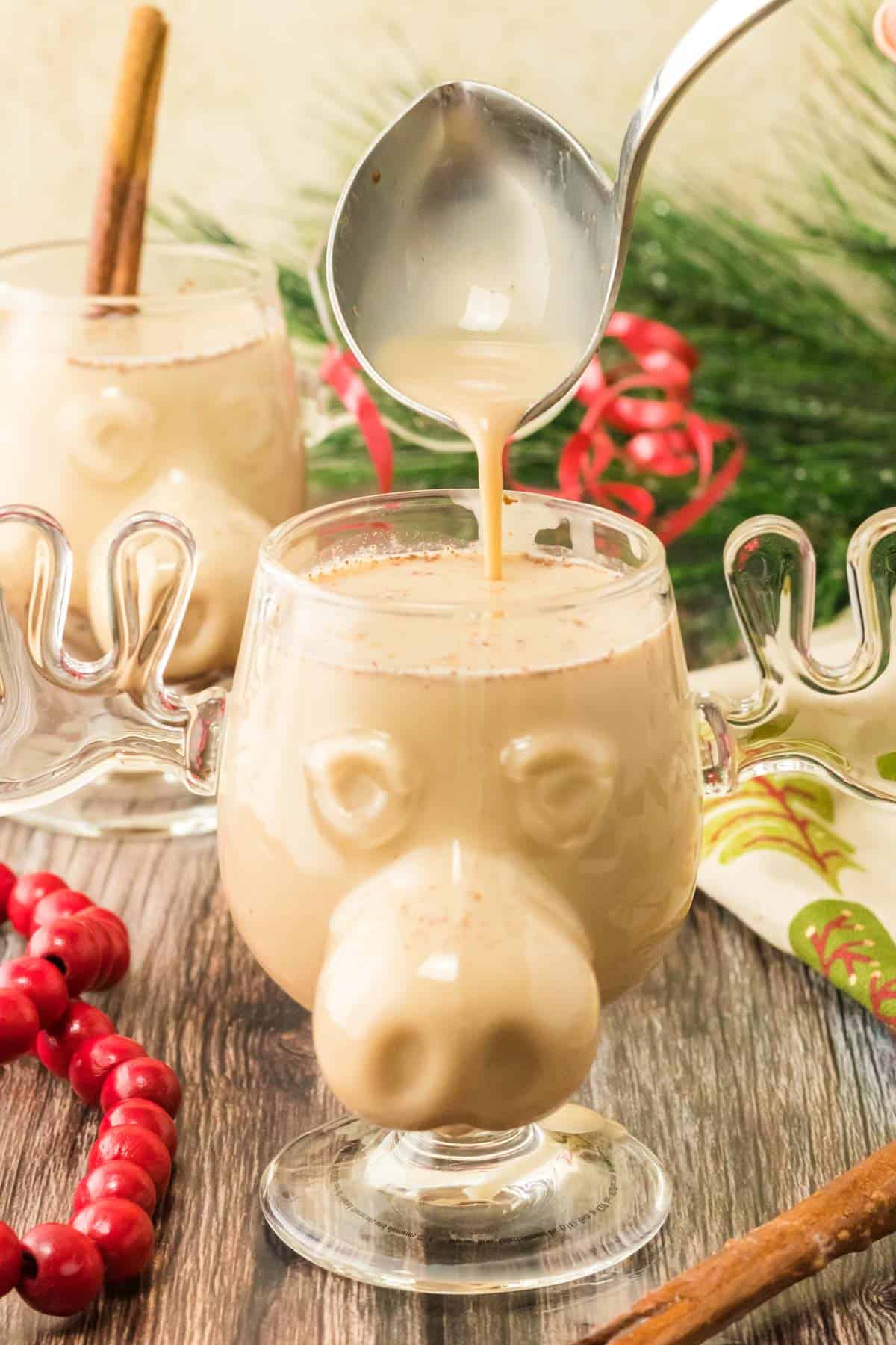 Pouring homemade eggnog with a silver ladle into a glass cup.