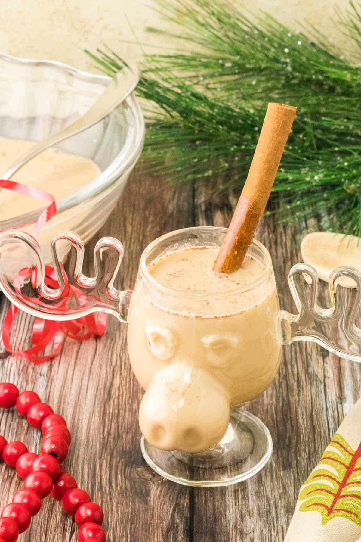 A cup of homemade eggnog in a moose cup garnished with a cinnamon stick.