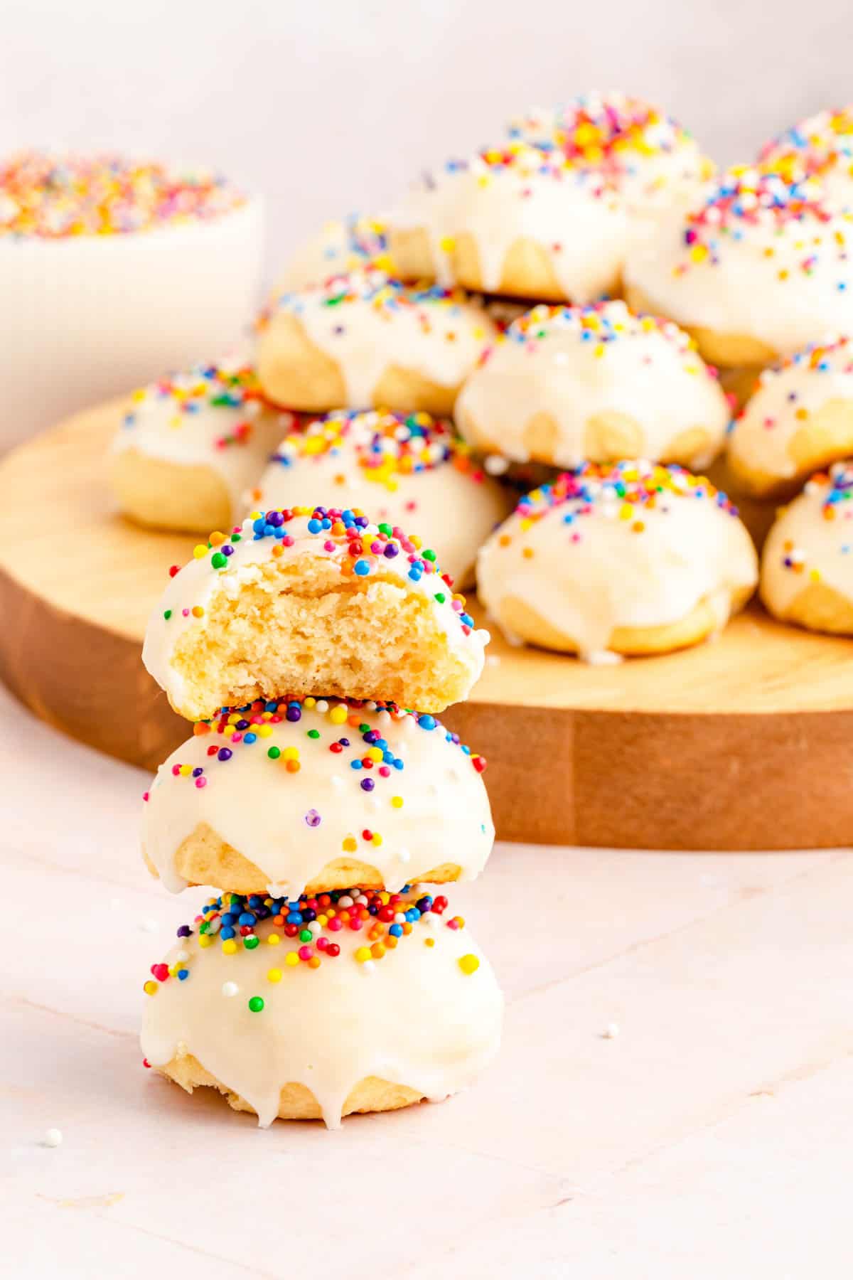 A stack of three Italian ricotta cookies with glaze and sprinkles, with bite taken out of the top cookie.