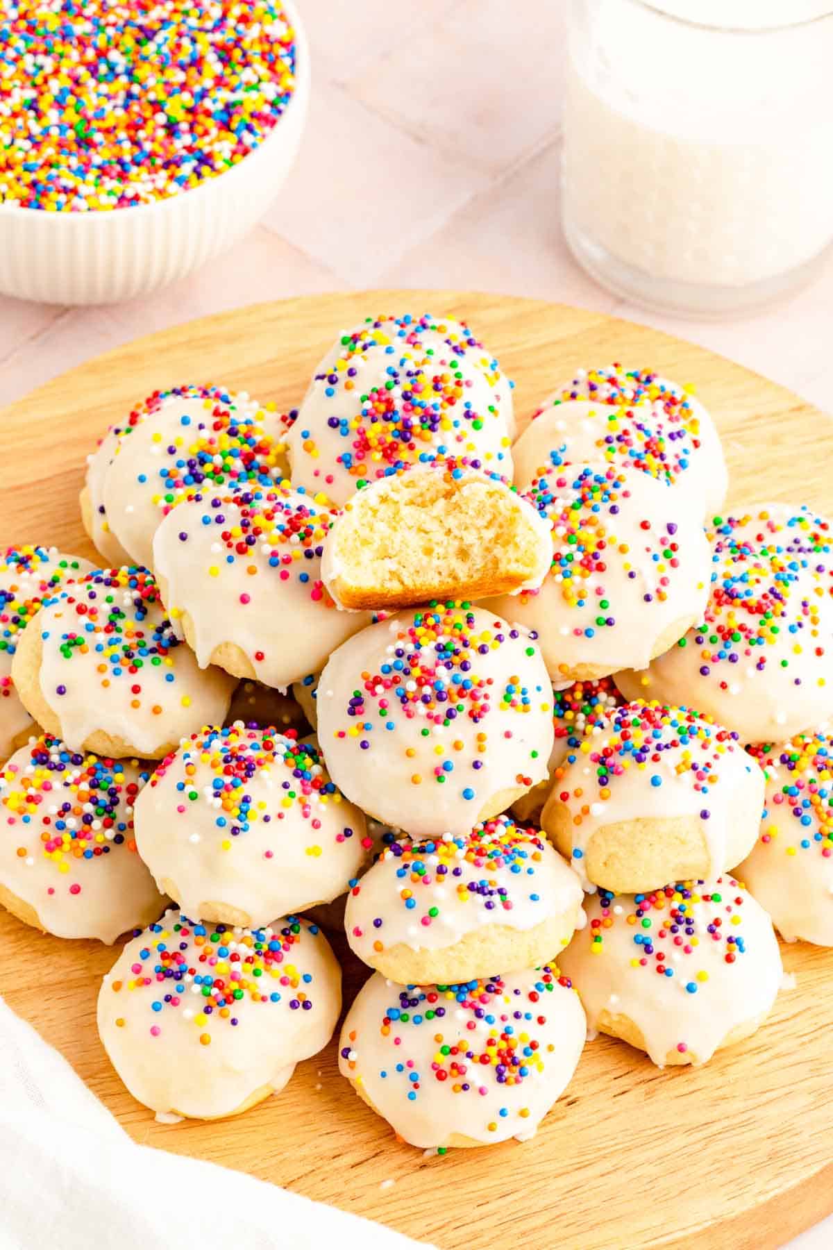 A wooden board filled with Italian Ricotta Cookies topped with glaze and colorful sprinkles.