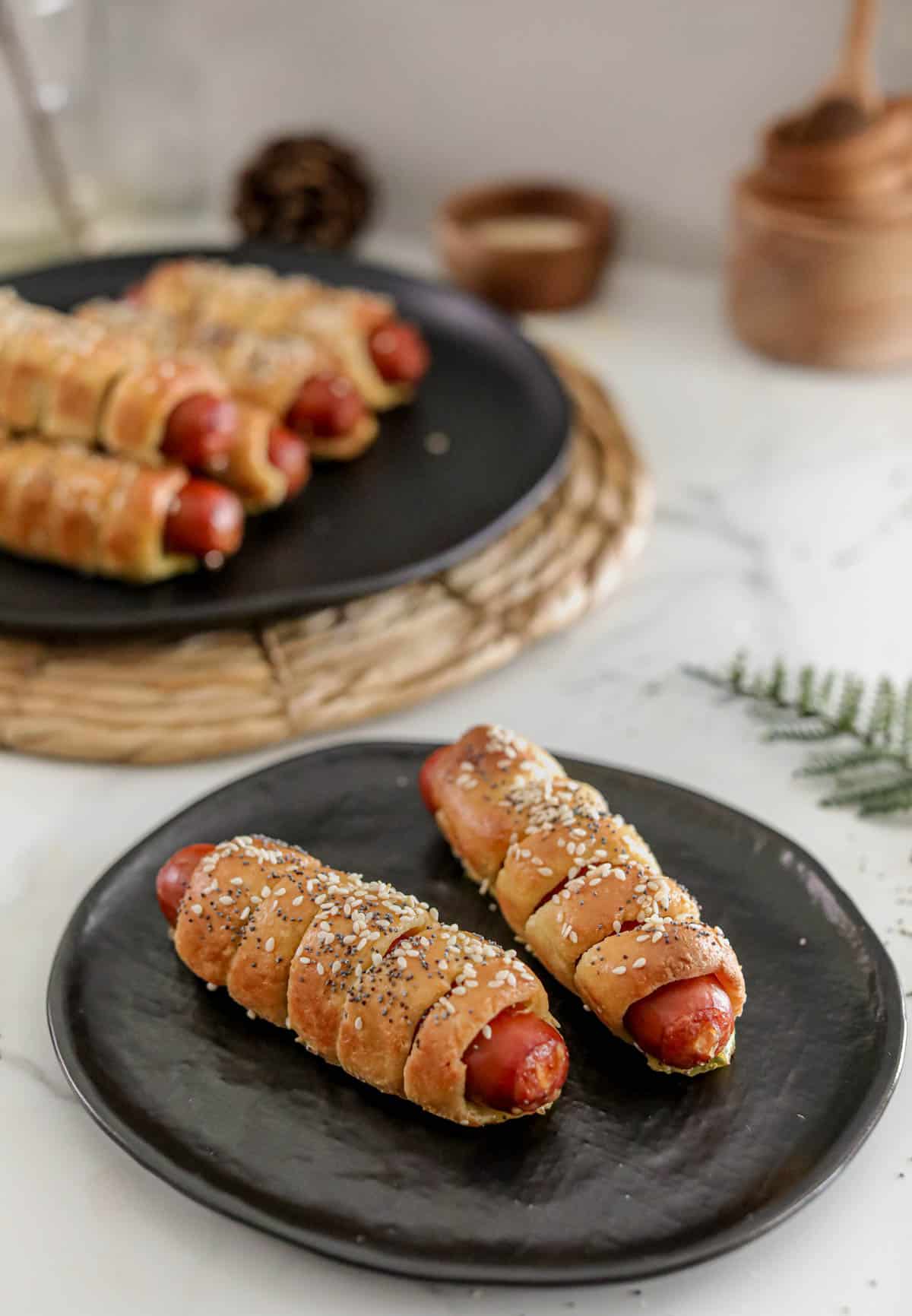 A black plate with 2 keto bagel dogs with a serving plate filled with more in the background.