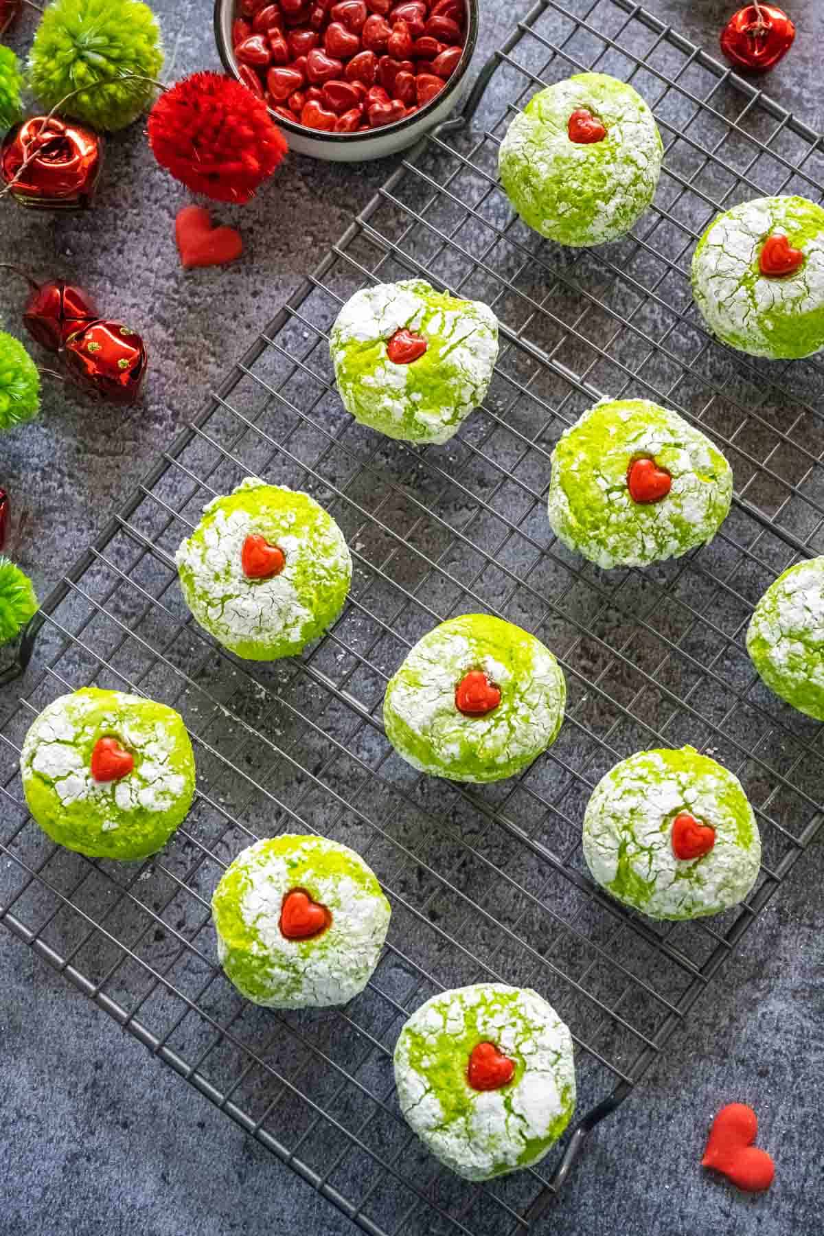 A cooling rack lines with green grinch cookies on a grey marble table.