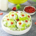 A white serving plate stacked with bright green grinch themed cookies with a heart in the middle.