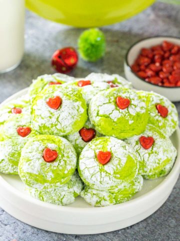 A white serving plate stacked with bright green grinch themed cookies with a heart in the middle.