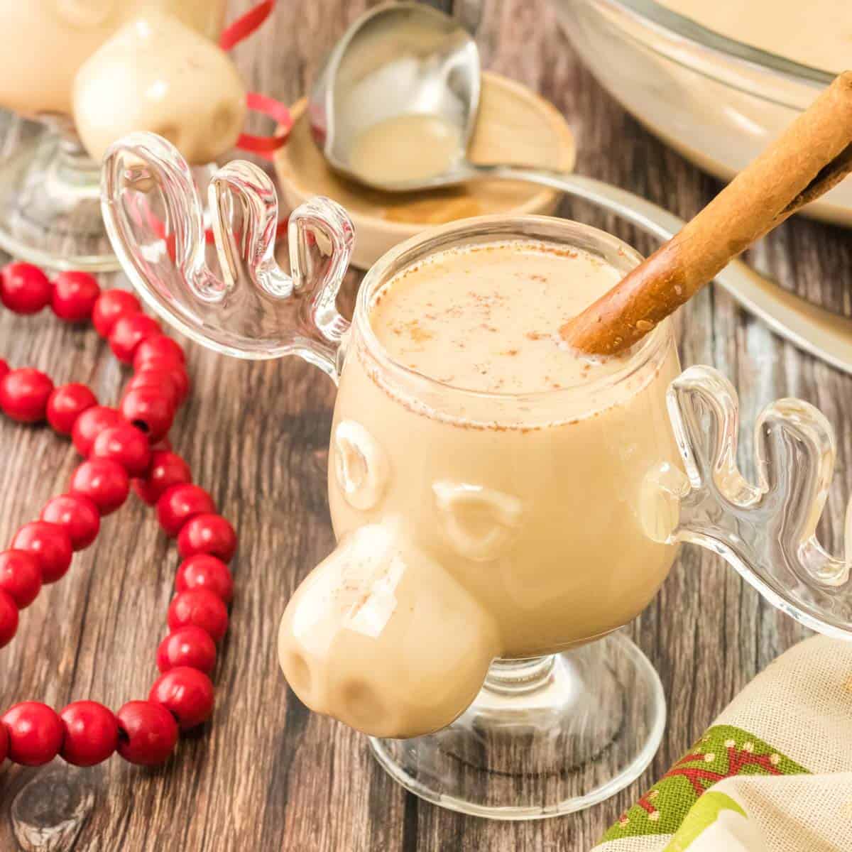 A cup of homemade eggnog in a moose cup garnished with a cinnamon stick.