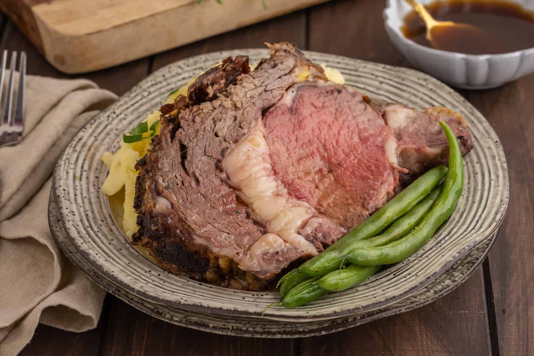 A delicious standing rib roast dinner set on a wooden table with a bowl of au jus in the background.