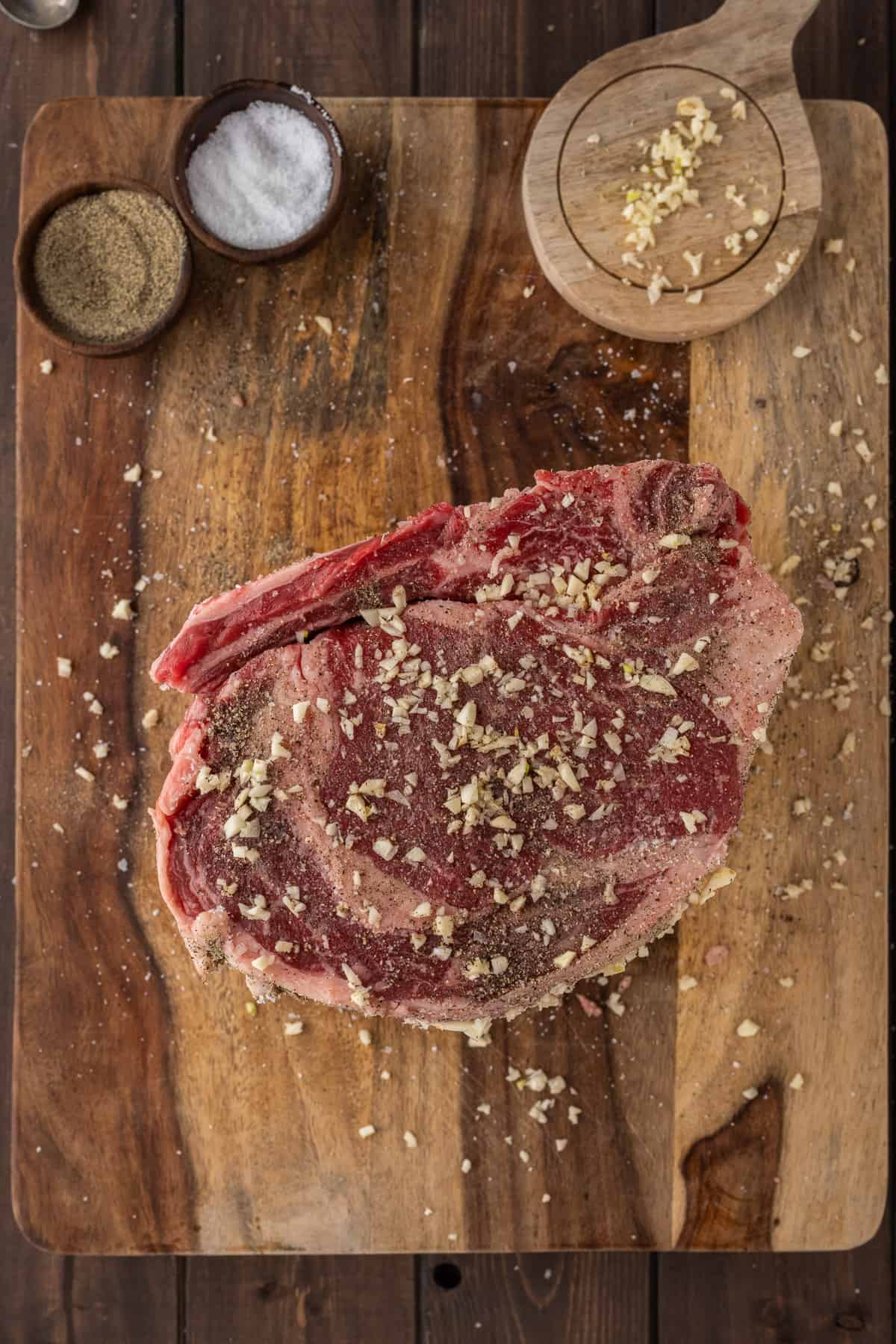 Prime rib being seasoning on the side with salt, pepper, and roughly mined garlic.