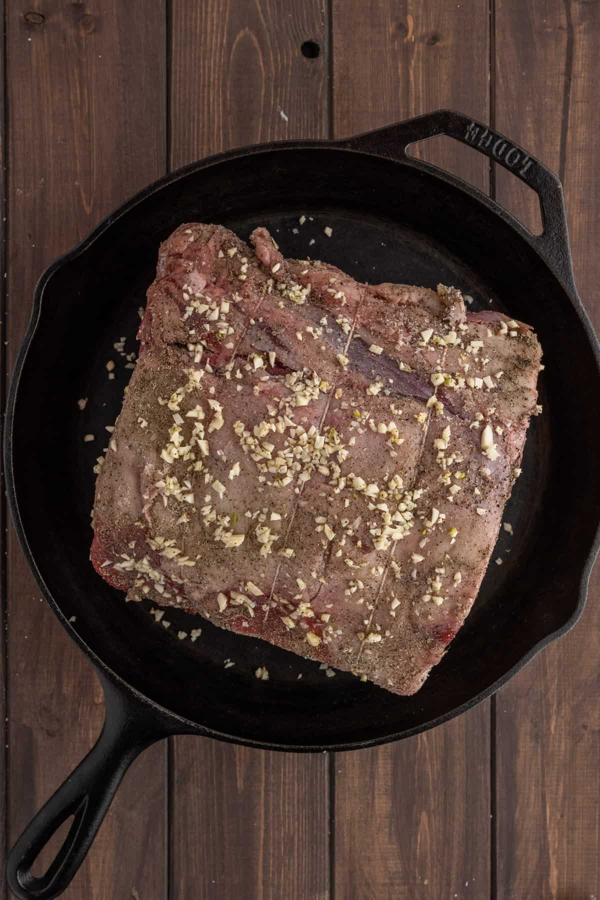 A seasoned standing rib roast bone side down in a large cast iron pan.