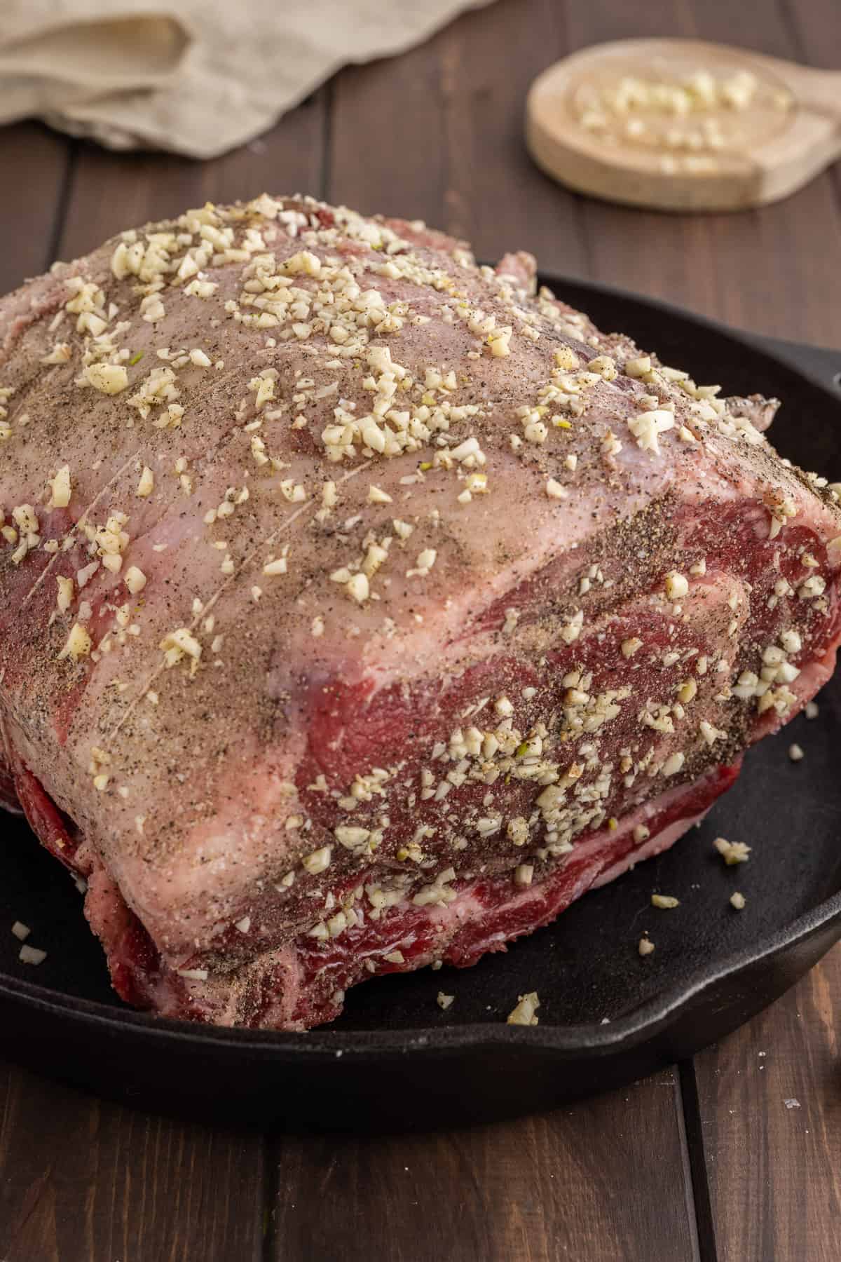 A side picture of a seasoning raw prime rib roast in a cast iron skillet.