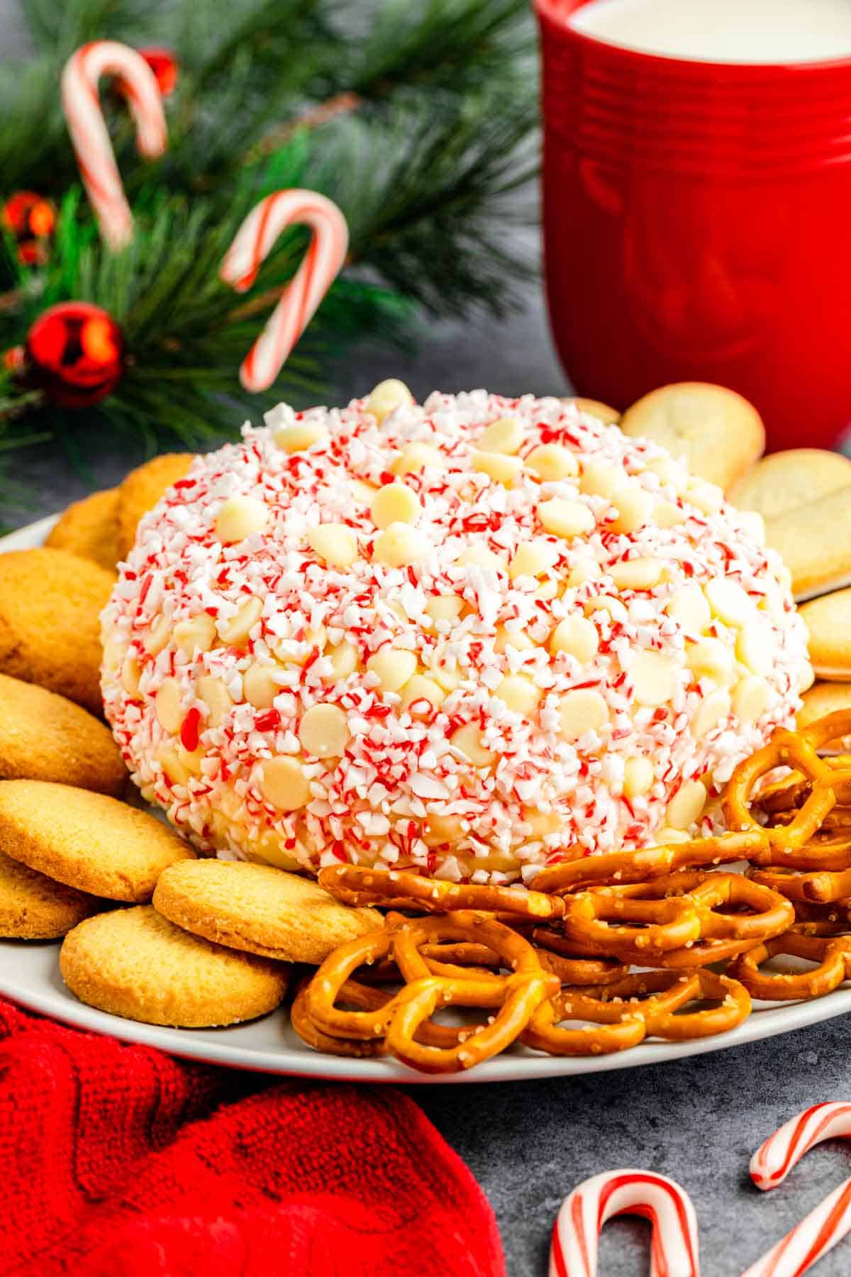 A peppermint cheesecake ball on a plate with pretzels and cookies decorated for Christmas.