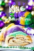 A slice of Mardi Gras King Cake on a white plate with red, gold, and purple beads scattered.
