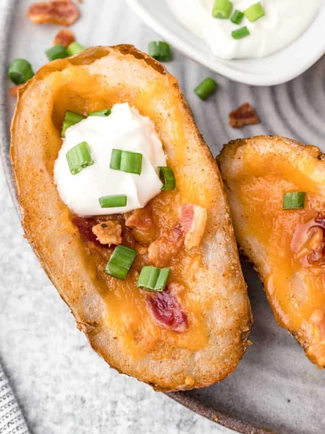 An up-close image of a baked potato skin layered with melted cheese, crispy bacon, sour cream, and sliced green onions.
